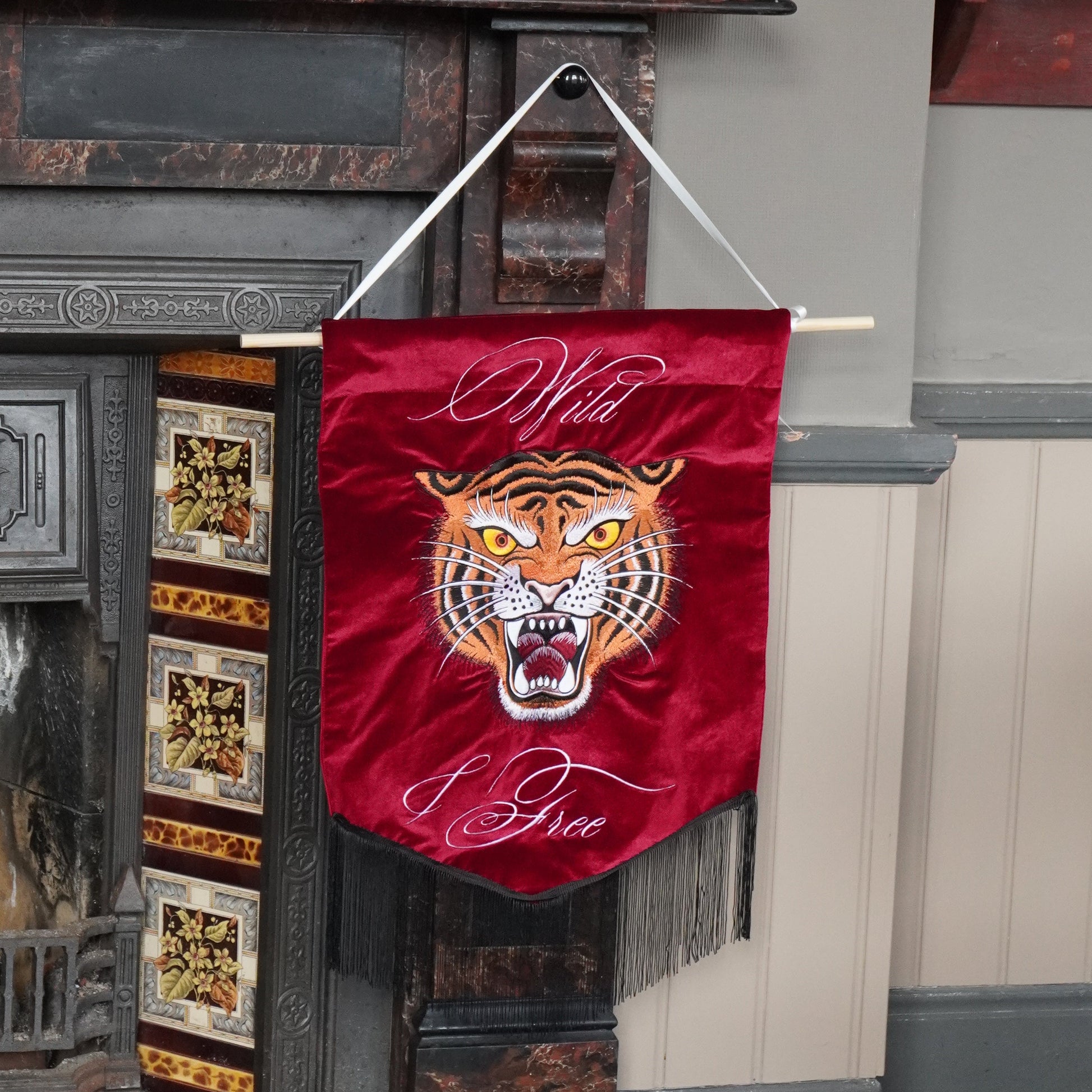 A red velvet wall banner featuring a tiger head graphic and the words 'Wild Fire' in white script, hanging from a wooden rod in front of a fireplace.