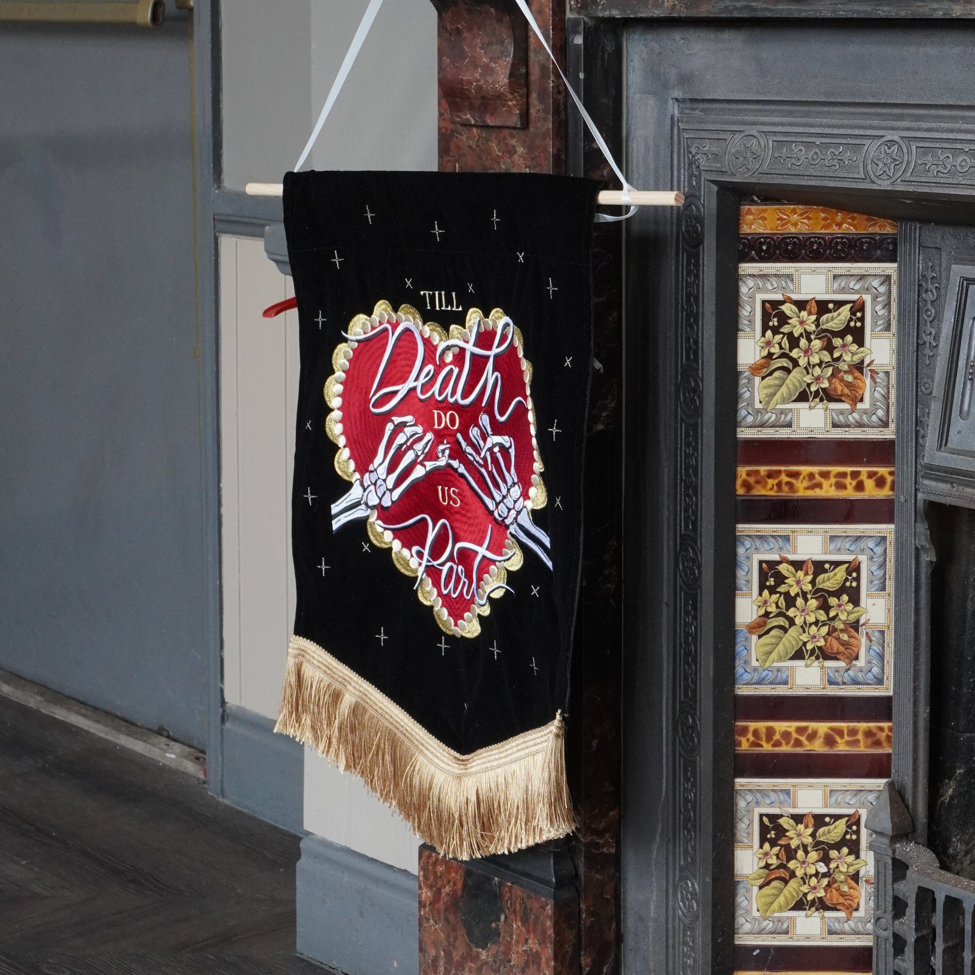 A black fabric banner with a red heart design and the words 'Death Art' hanging from a wooden rod in front of an old fireplace.