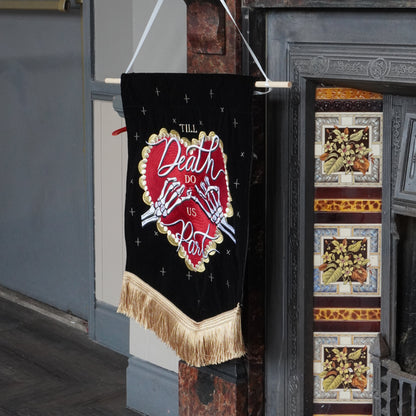 A black fabric banner with a red heart design and the words 'Death Art' hanging from a wooden rod in front of an old fireplace.