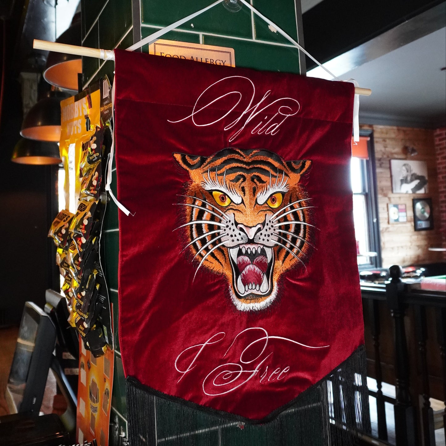 A red velvet bar banner featuring a roaring tiger graphic and the words 'Wild & Free' in white script, hanging from a metal rod in a restaurant or bar setting.