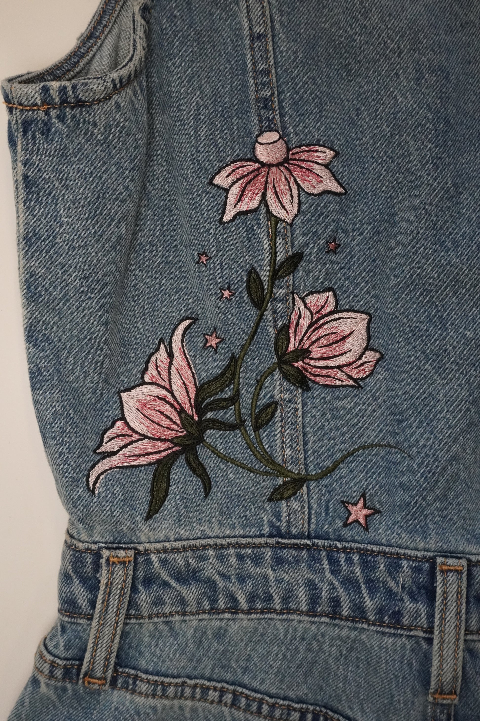 Close-up of a blue denim garment featuring embroidered pink flowers and green leaves on the front.
