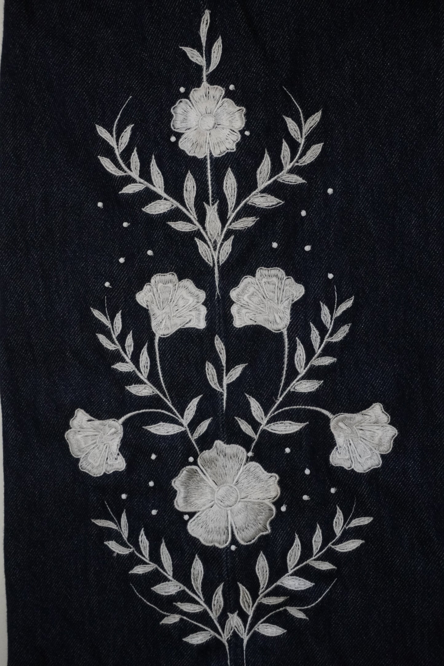 A close-up of a dark navy blue fabric featuring a detailed white floral and leaf embroidery design.