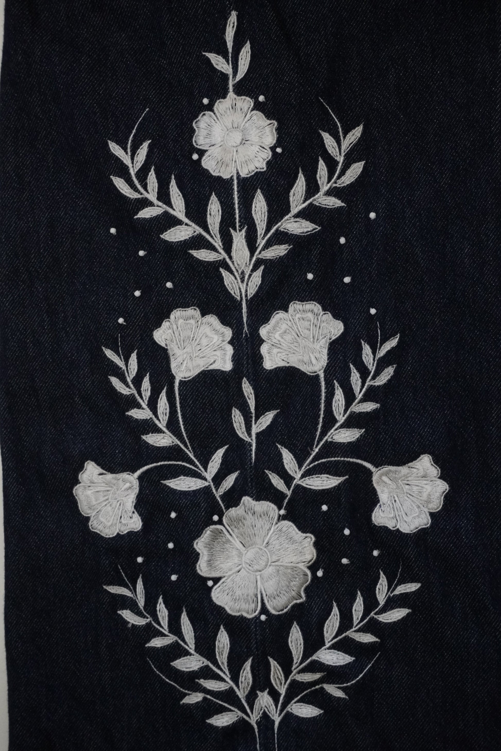 A close-up of a dark navy blue fabric featuring a detailed white floral and leaf embroidery design.