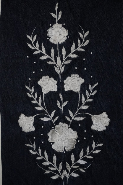 A close-up of a dark navy blue fabric featuring a detailed white floral and leaf embroidery design.