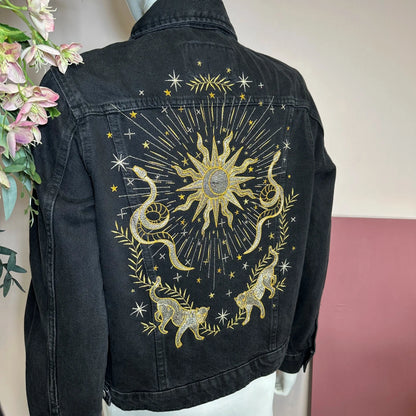 Black denim jacket with gold celestial design on a mannequin against a neutral background.