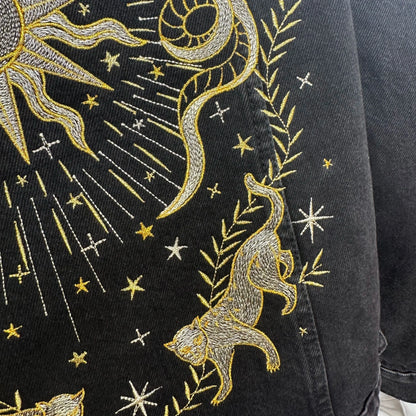 Embroidered design on a black fabric with gold stars, moon, sun, and cheetah.