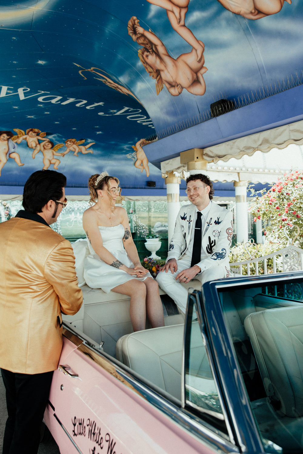 Couple getting married by Elvis in a vintage car in Vegas. The groom is wearing a bespoke embroidered casino, vegas, western themed suit. 