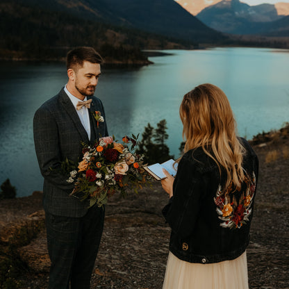 Bride wearing a custom floral embroidered bridal denim jacket overlooking mountains on her wedding day.