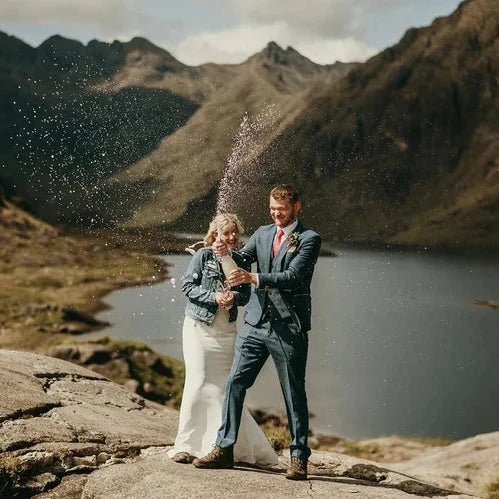 Couple celebrating with a bottle of champagne in a mountainous landscape in The Isle of Skye for a wedding elopement 