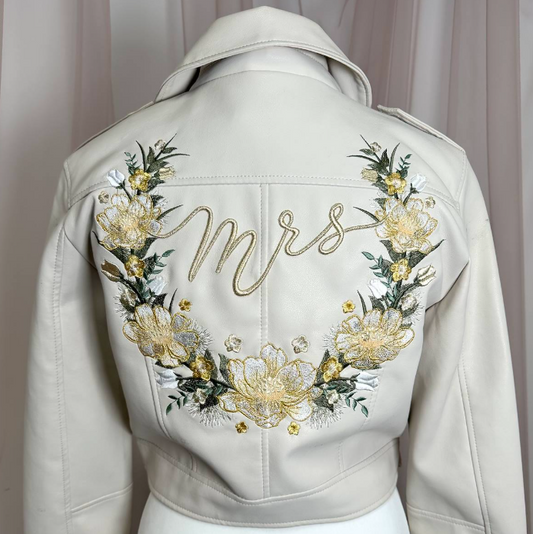 An off-white faux leather cropped jacket displayed on a white mannequin, showing the back decorated with a large floral wreath and the word 'Mrs' in gold cursive embroidery.