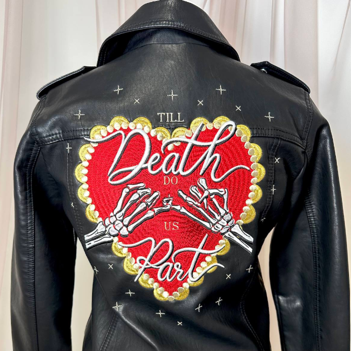 Black leather jacket shown from the back on a mannequin, featuring a large red heart graphic with skeleton hands and the text 'Till Death Do Us Part' in white script and block lettering, with small white star accents.