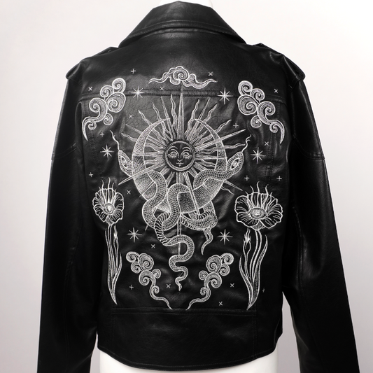 Black leather jacket displayed on a white mannequin torso, showing the back with a large white celestial graphic featuring a sun, snake, stars, and floral motifs.
