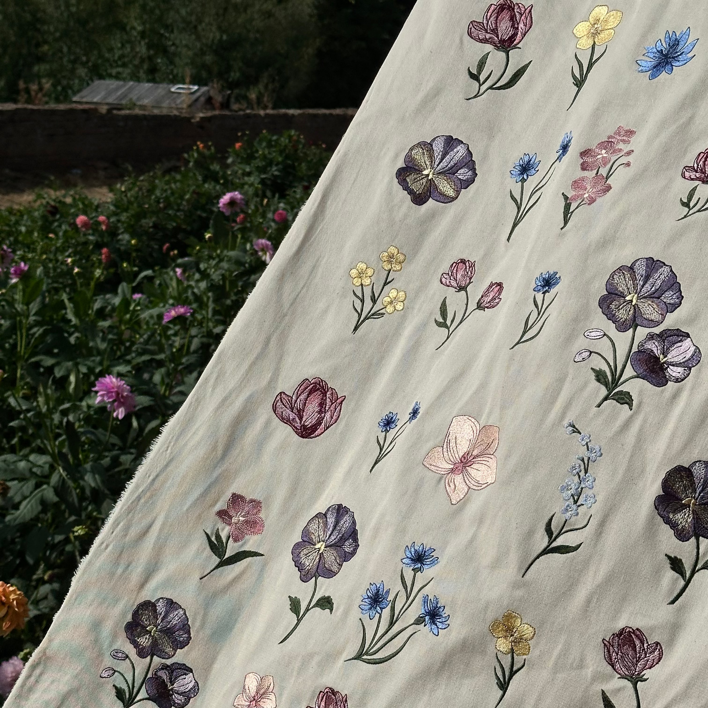 A collection of beautifully embroidered machine files on to a canvas banner, placed in a flower garden.