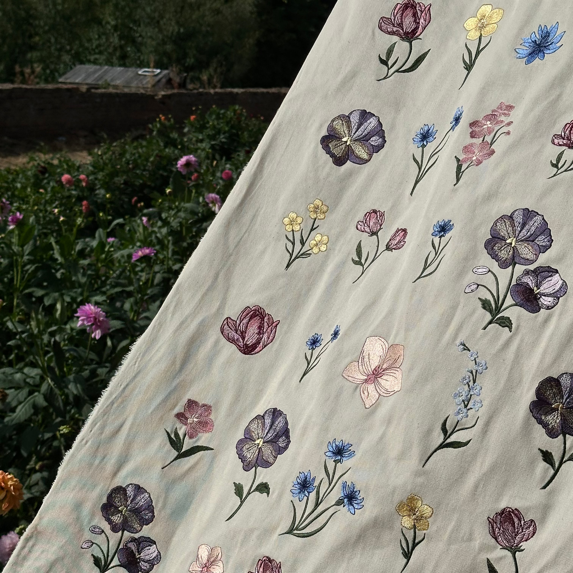 A collection of beautifully embroidered machine files on to a canvas banner, placed in a flower garden.