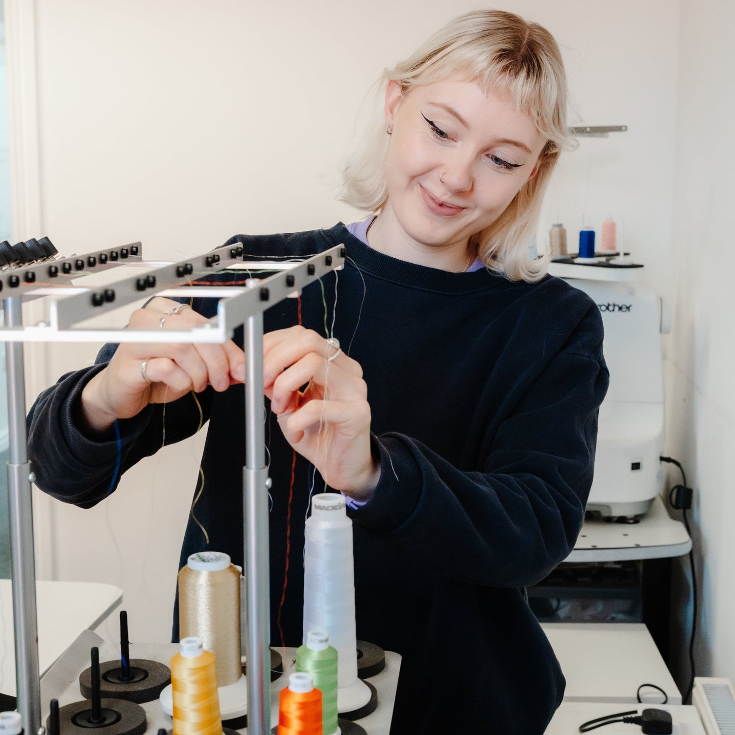 Staff member threading an industrial embroidery machine, using the Tajima Sumo Machine 
