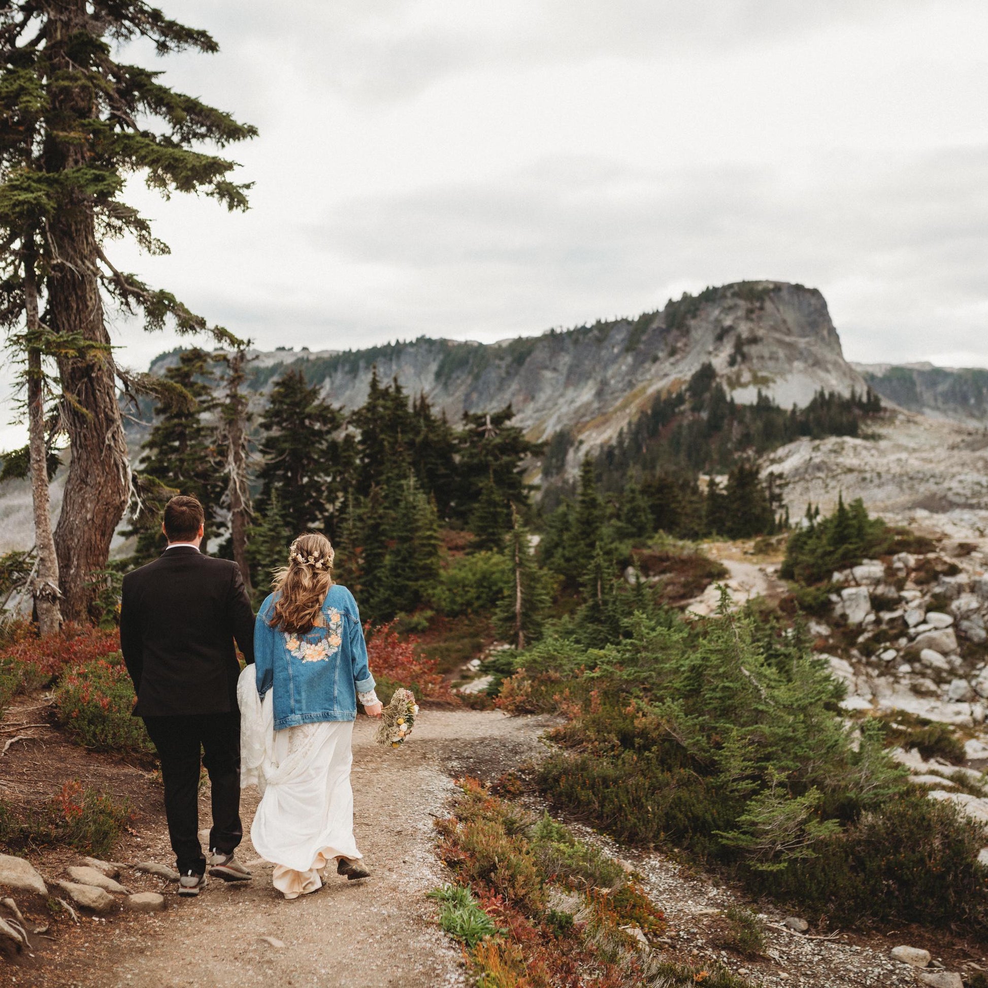 Two people walking on a trail with mountains and trees in the background